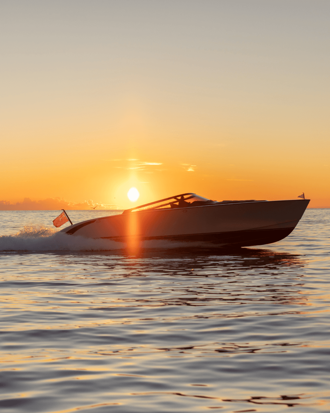 A sleek speedboat gliding on calm waters during a vibrant sunset, with the sun casting an orange glow on the horizon.