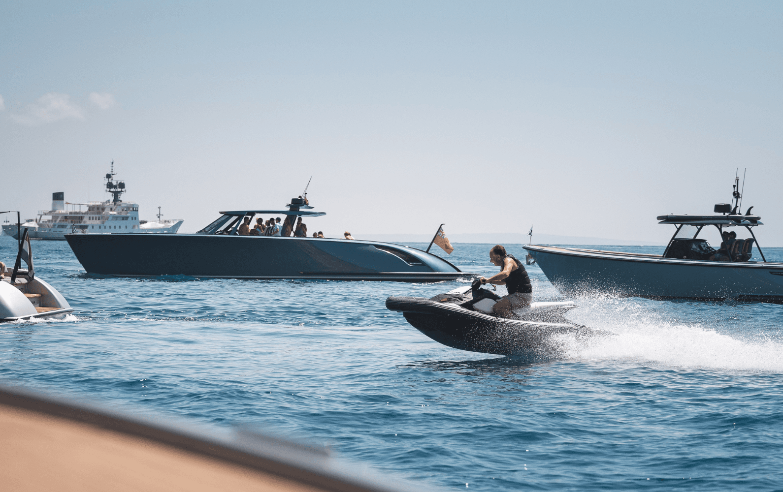 A person rides a jet ski on the sea near several yachts on a clear day.