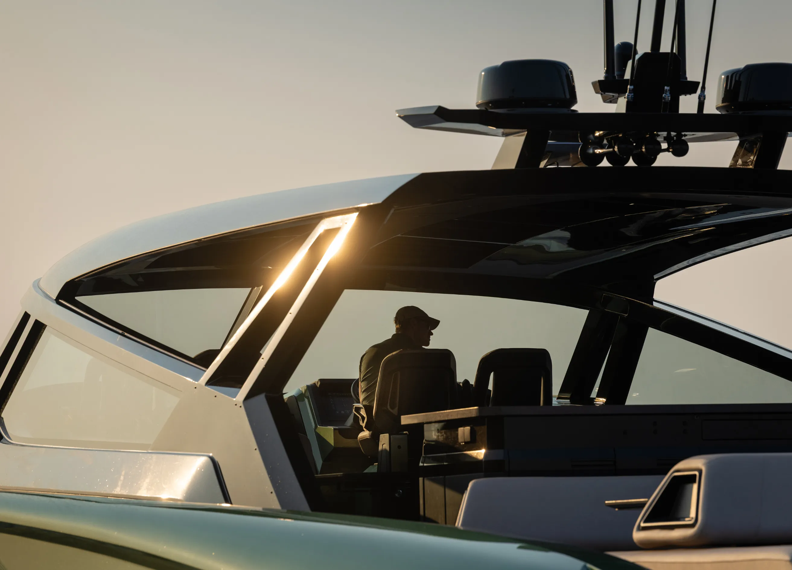 A person sits inside a modern yacht cabin, silhouetted by the setting sun, surrounded by sleek, angular lines and navigational equipment.