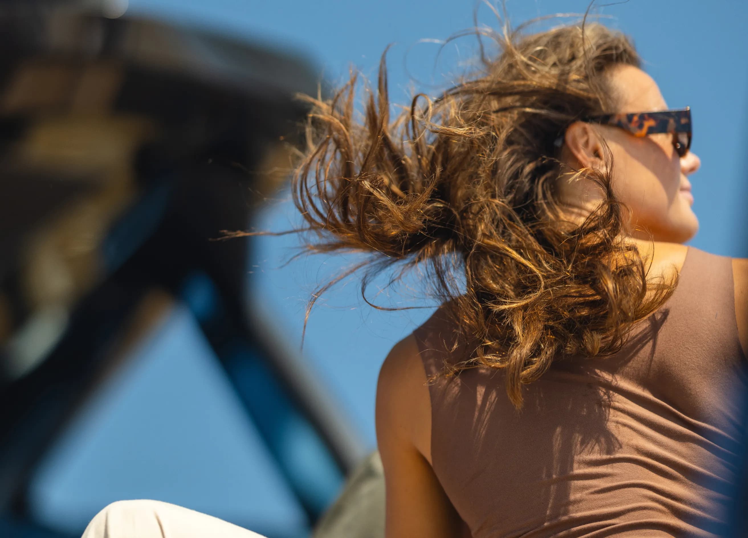 A person with sunglasses and long hair blowing in the wind, enjoying a sunny day.