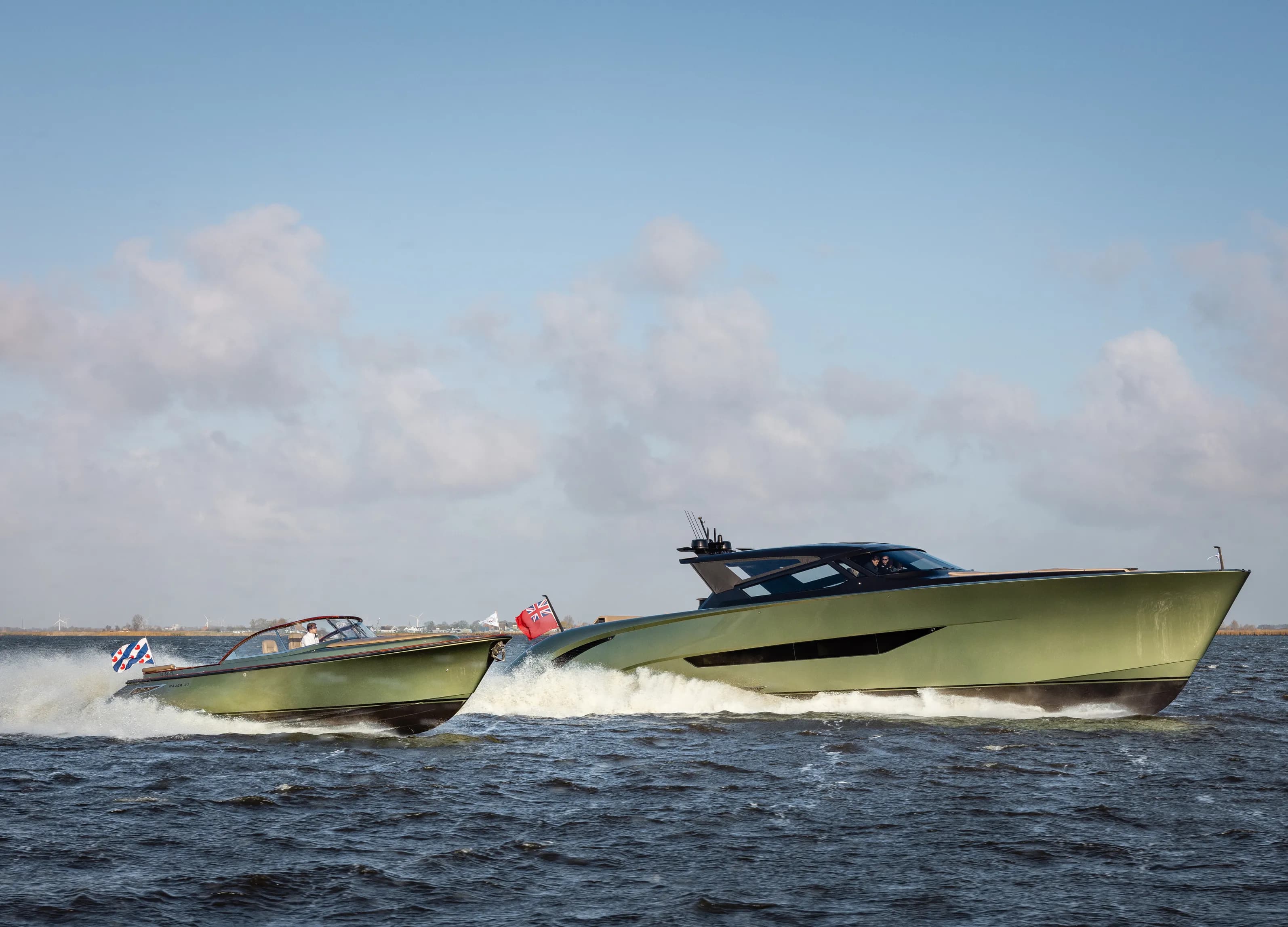 Two speedboats with green hulls cruising on a sunny day across choppy waters, flags waving at the sterns.